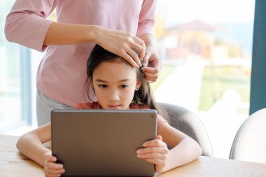 Asian woman and her daughter using tablet computer while spending time together at home