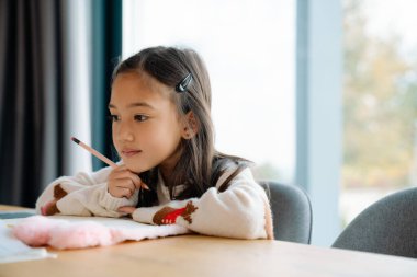 Asian girl doing homework while sitting at table at home