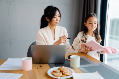 Asian girl doing homework with her mother in kitchen at home