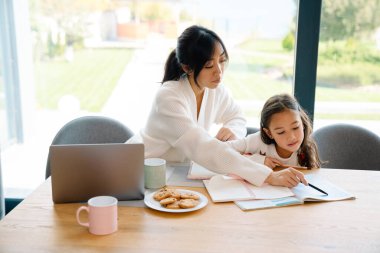 Asian girl doing homework with her mother in kitchen at home