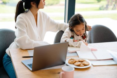 Asian girl doing homework with her mother in kitchen at home