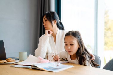 Asian girl doing homework with her mother in kitchen at home