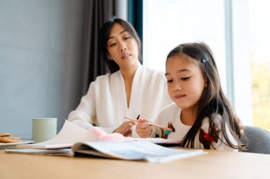 Asian girl doing homework with her mother in kitchen at home