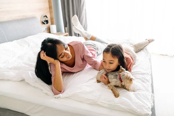 Азійська Мати Дочка Посміхаються Лежачи Ліжку Своїм Собакою Вдома — стокове фото
