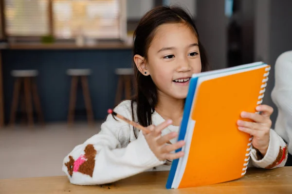 Asiatisches Mädchen Lächelt Und Macht Hausaufgaben Während Hause Tisch Sitzt — Stockfoto