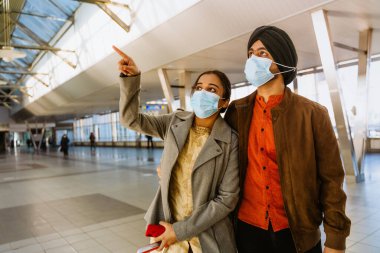 Yüz maskesi takan Hintli çift havalimanında sarılıyor ve işaret ediyor.