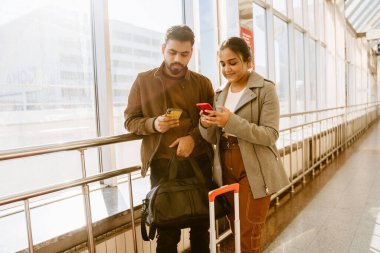 Genç Hintli çift havaalanında beklerken cep telefonu kullanıyor.