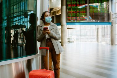 Tren istasyonunda cep telefonu kullanan yüz maskesi takan Hintli kadın.