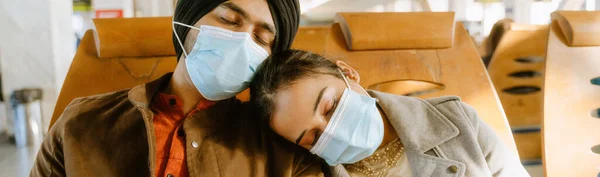 Indian couple wearing face masks sleeping while sitting in airport indoors