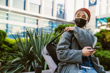 Asyalı çocuk şehir caddesinde cep telefonu ve kulaklık kullanıyor.