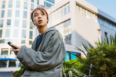 Şehir caddesinde cep telefonu ve kulaklık kullanan Asyalı bir çocuk.