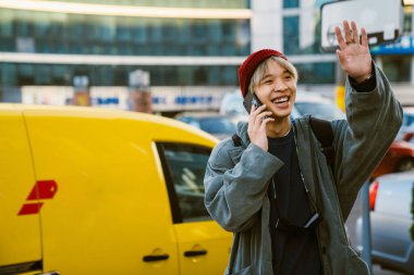 Şehir caddesinde cep telefonuyla konuşurken gülen ve el kol hareketi yapan Asyalı çocuk.