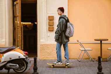 Asyalı çocuk şehir caddesinde kaykay yaparken müzik dinliyor.