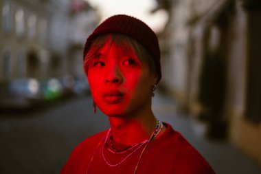 Asyalı çocuk şehir sokaklarında dikilirken yana bakıyor.