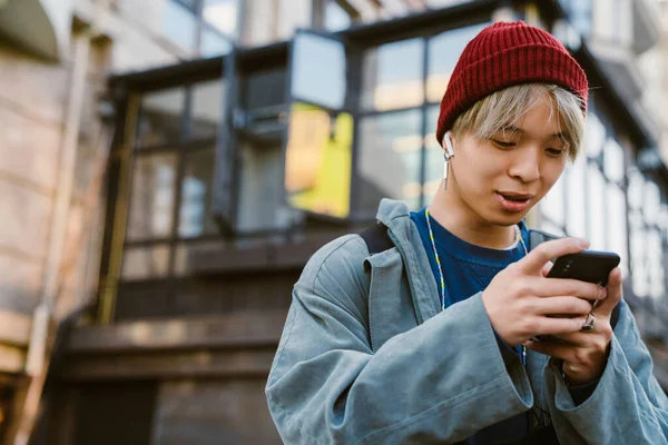 stock image Asian boy wearing hat using mobile phone and earphones on city street