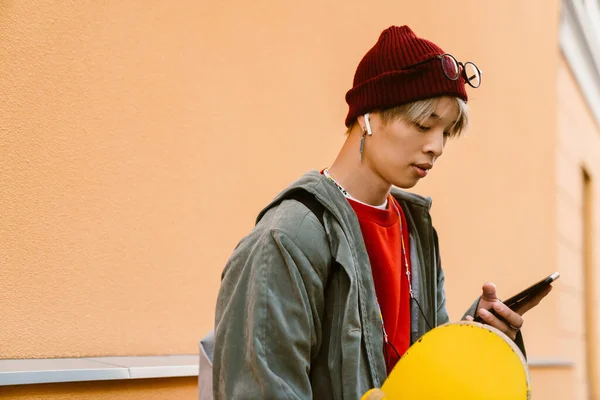Asijské Chlapec Skateboard Pomocí Mobilního Telefonu Sluchátek Ulici — Stock fotografie