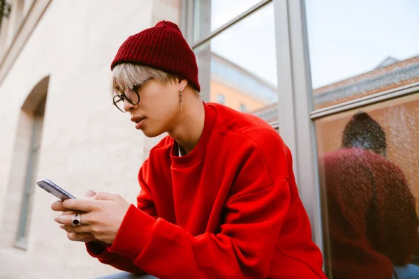 Asijské Chlapec Nosí Brýle Pomocí Mobilního Telefonu Zatímco Sedí Zdi — Stock fotografie