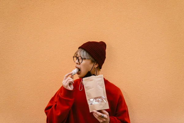 屋外で壁に立っている間に眼鏡をかけクッキーを食べるアジアの少年 — ストック写真