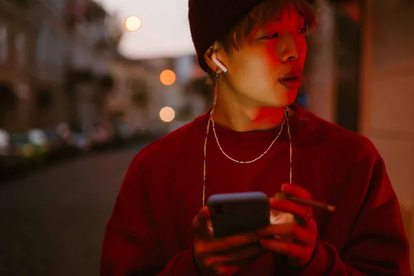 Asijské Chlapec Sluchátkách Pomocí Mobilního Telefonu Při Kouření Ulici — Stock fotografie