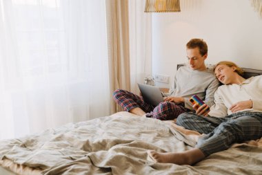 Genç eşcinsel çift evde dinlenirken cep telefonu ve laptop kullanıyor.