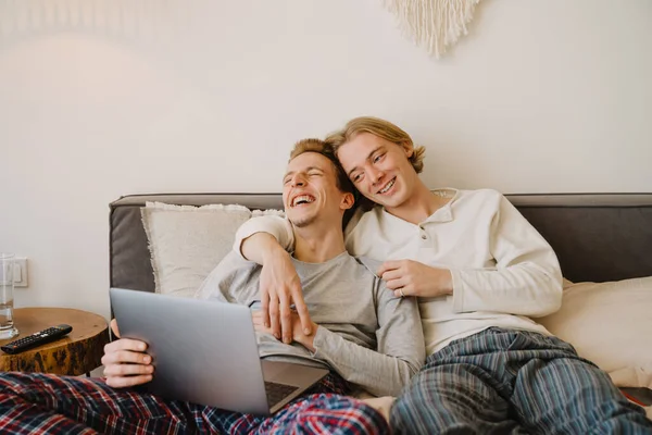 Unga Homosexuella Par Skrattar Och Använder Laptop Medan Vilar Sängen — Stockfoto
