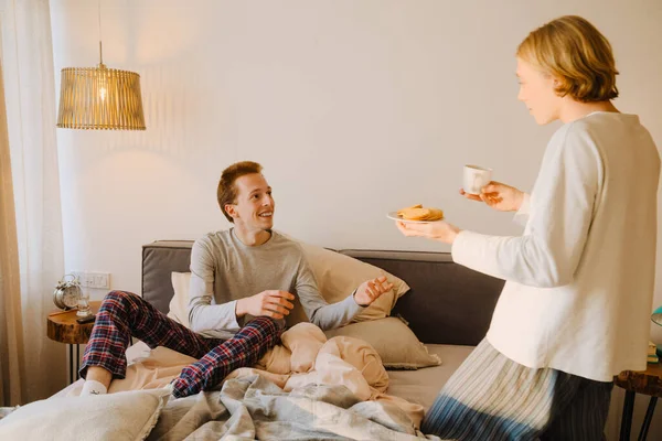 stock image Young gay couple smiling and having breakfast while resting in bed at home