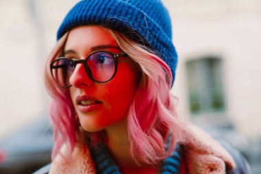 Gözlüklü genç beyaz kadın poz veriyor ve şehir sokağına bakıyor.