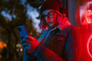 Şehir caddesinde yürürken müzik dinleyen ve cep telefonu kullanan genç bir kadın.