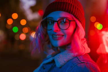 Gözlüklü genç beyaz kadın gülümsüyor ve kameraya bakıyor.