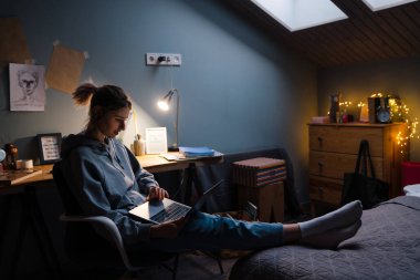 Tünel yüzüklü beyaz kız evdeki koltukta otururken dizüstü bilgisayar kullanıyor.