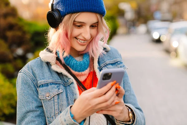 stock image Young woman listening music and using cellphone while walking in park outdoors