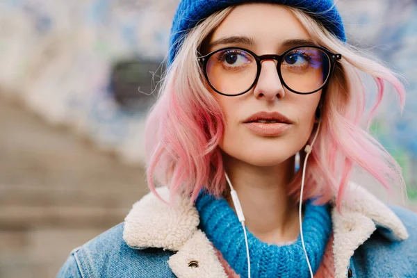 Young woman in eyeglasses listening music while standing outdoors