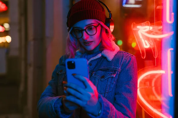 stock image Young woman listening music and using cellphone while walking at city street