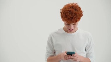 Beyaz stüdyoda telefonla mesajlaşan komik kızıl saçlı genç adam.