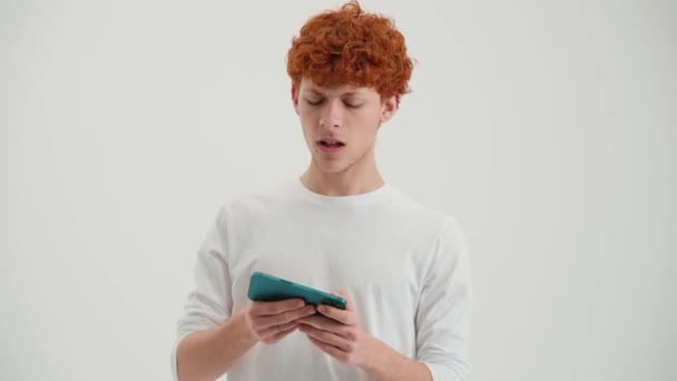 Όμορφος Κοκκινομάλλης Νεαρός Άνδρας Παίζει Παιχνίδι Στο Τηλέφωνο Στο Λευκό — Αρχείο Βίντεο