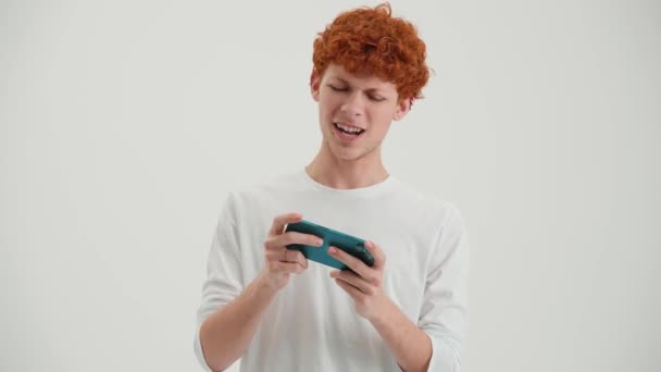 Веселий Рудий Молодий Чоловік Грає Гру Мобільному Телефоні Білій Студії — стокове відео