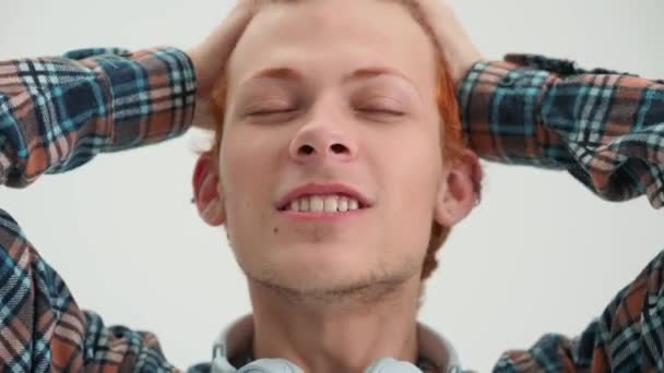 陽気な赤い髪の若い男彼の髪を引っ掻いて 白いスタジオでカメラを見て — ストック動画