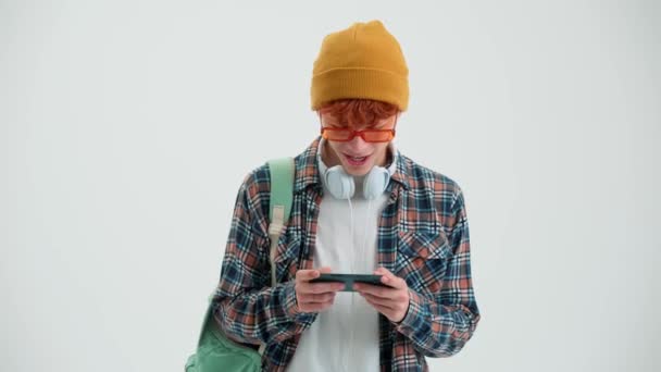 Sırt Çantalı Kızıl Saçlı Adam Beyaz Stüdyoda Cep Telefonuyla Oyun — Stok video
