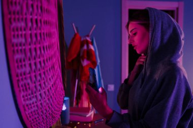 Beyaz kız evde aynaya bakarken cep telefonundan selfie çekiyor.