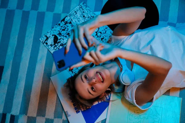 一个白人女孩躺在家里的地板上 一边用手机自拍 — 图库照片