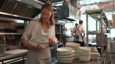 Lokanta mutfağında tabak istifleyen neşeli sarışın kadın şef.