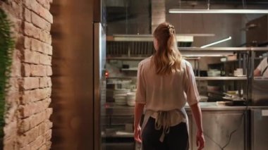 Mutfak mutfağında yürüyen ve tabakları istifleyen mutlu sarışın kadın şef.