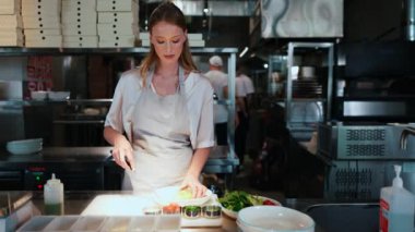 Ciddi sarışın kadın şef restoran mutfağında salata hazırlıyor.