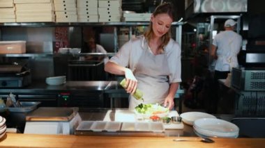 Mutlu sarışın kadın şef restoran mutfağında salata hazırlıyor.