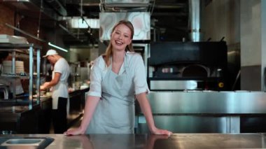 Sarışın kadın aşçı restoran mutfağında kameraya bakıyor.