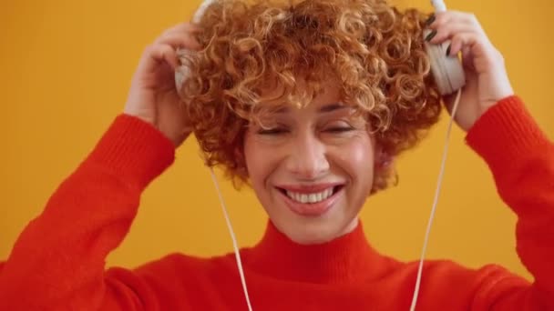 Sonriente Pelirroja Adulta Rizada Escuchando Música Auriculares Bailando Estudio Amarillo — Vídeos de Stock