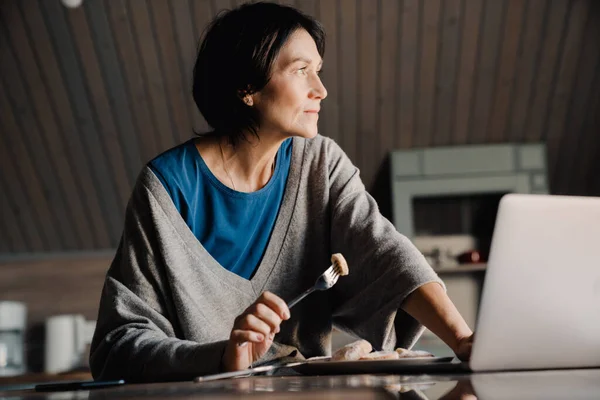 Vit Mogen Kvinna Använder Laptop Medan Äter Frukost Hemma — Stockfoto
