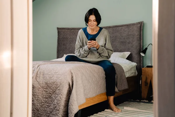 Wanita Kulit Putih Dewasa Menggunakan Ponsel Saat Duduk Tempat Tidur — Stok Foto