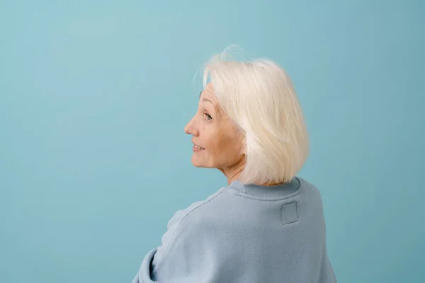 身穿蓝色套头衫的漂亮老年妇女背靠在孤立的蓝色背景上 — 图库照片