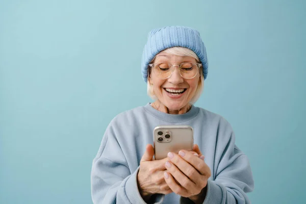 Счастливая Улыбающаяся Пожилая Женщина Зимней Шляпе Очках Держа Руках Телефон — стоковое фото